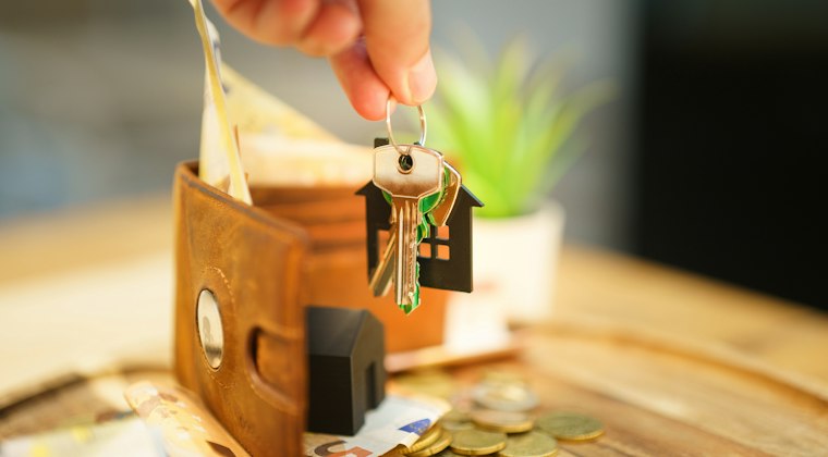 Hand holding keys with house charm and wallet